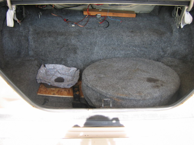 Car trunk with spare tire and some insulation material. Wiring is visible near the trunk lid