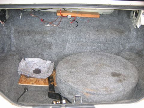 1985 Ford LTD Crown Victoria - The trunk of a car shows a spare tire, exposed wiring, and a wooden platform with insulation material.