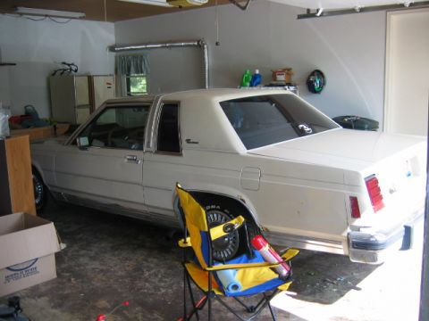 1985 Ford LTD Crown Victoria - Three-quarter rear view of a cream two-door Ford LTD sedan/coupe sitting in a home garage with the front end on jack stands and a wheel rem…
