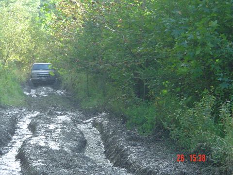 1989 Ford Bronco - A vehicle navigates a difficult, muddy path through a wooded area.
