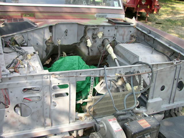 Vehicle engine bay with exposed metal, wiring, and a green tarp covering parts