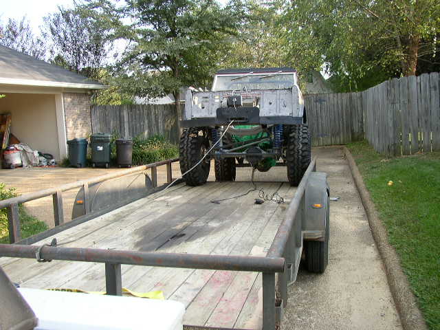 Off-road vehicle with large tires on trailer, rear view. Green differential visible