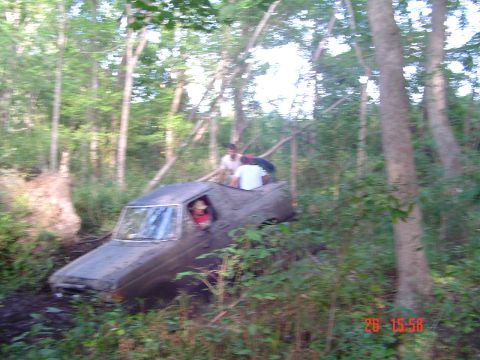 1989 Ford Bronco - A vehicle is stuck in the mud while people are on and in it, surrounded by trees.