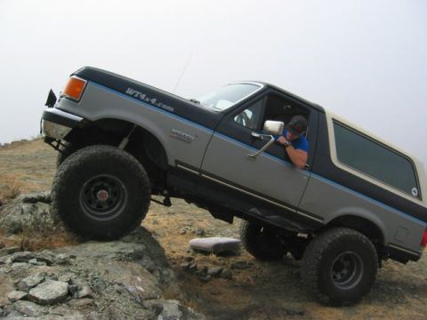 1989 Ford Bronco - A driver leans out the window of a modified Ford Bronco navigating a rocky incline.
