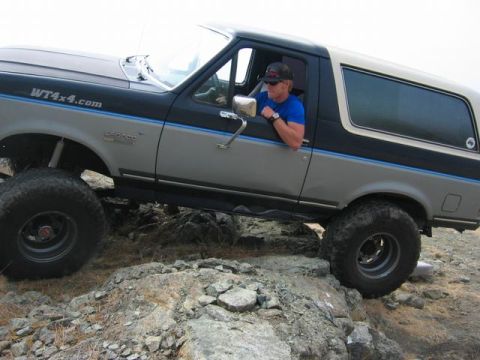 1989 Ford Bronco - Driver in blue shirt leans out window of a 1989 Ford Bronco navigating rocky terrain.