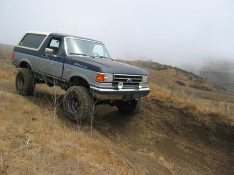 1989 Ford Bronco - This lifted Ford Bronco is navigating a steep, dusty trail on a foggy day.