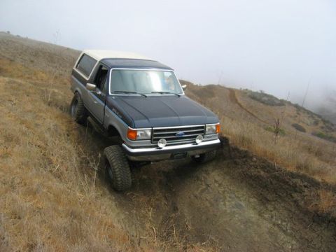 1989 Ford Bronco - A Ford Bronco navigates a muddy, off-road trail on a foggy day.