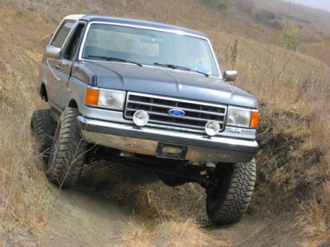 1989 Ford Bronco - 1989 Ford Bronco navigating an off-road trail with steep inclines and dry vegetation.