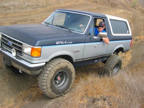 1989 Ford Bronco - This lifted Ford Bronco navigates a dry, grassy hillside with its driver looking on.
