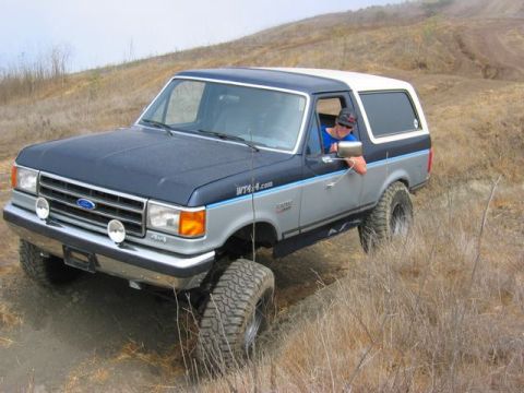 1989 Ford Bronco - A man drives a Ford Bronco on a dirt trail with dry grass and hills in the background.