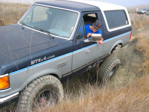 1989 Ford Bronco - A Ford Bronco navigates a dirt trail with a driver looking out the window. Another vehicle is visible in the distance.