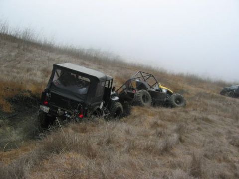 1989 Ford Bronco - Two off-road vehicles navigate a foggy, grassy hillside.