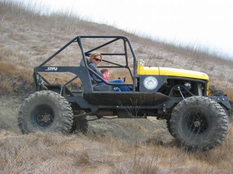 1989 Ford Bronco - Custom off-road buggy with roll cage and large tires is driven on a grassy hill.