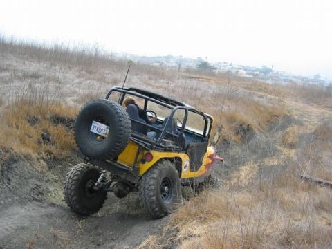 1989 Ford Bronco - A yellow Jeep navigates a steep, dry, grassy hill on an off-road trail.