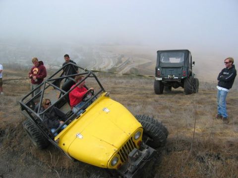 1989 Ford Bronco - Two off-road vehicles, a yellow buggy and a green Jeep, are on a grassy hillside with several people observing.