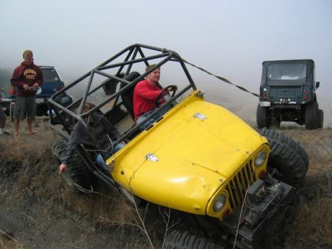 1989 Ford Bronco - A yellow off-road buggy with a roll cage is stuck on a muddy incline, being towed by a green Jeep.
