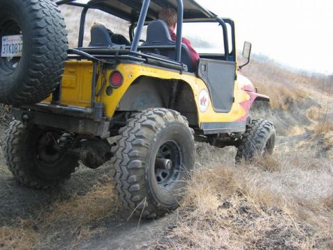 1989 Ford Bronco - A yellow off-road vehicle navigates a dry, grassy trail with large, tires.