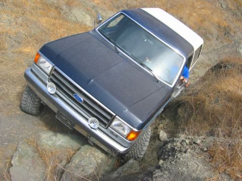 1989 Ford Bronco - Ford Bronco navigates a challenging rocky incline on a dry, grassy hillside.