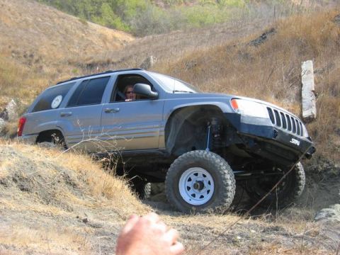 1989 Ford Bronco - Modified Jeep Grand Cherokee tackling an off-road course with a driver visible inside.