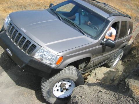 1989 Ford Bronco - A gray Jeep Grand Cherokee navigates a challenging off-road obstacle, demonstrating its articulation.