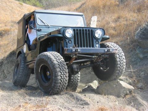1989 Ford Bronco - A green Jeep CJ-5 navigates a rocky trail with its tires angled on boulders.