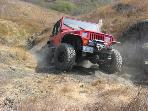 1989 Ford Bronco - Red Jeep Wrangler navigating a dusty off-road trail with steep inclines.
