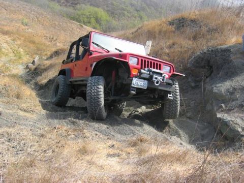 1989 Ford Bronco - A red Jeep Wrangler navigates a challenging off-road trail with steep inclines and rocky terrain.