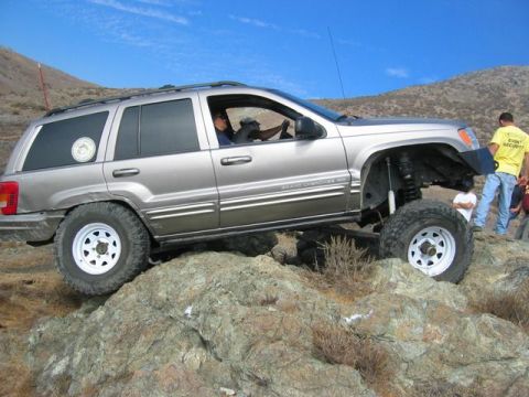 1989 Ford Bronco - A silver Jeep Grand Cherokee navigates a rocky terrain on a sunny day.