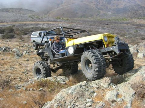 1989 Ford Bronco - A blue 1989 Ford Bronco follows a yellow Jeep off-road on a rocky, hilly terrain.