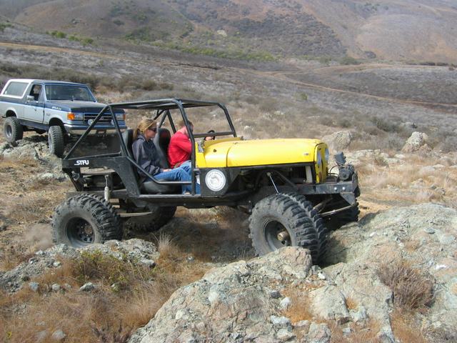 Two off-road vehicles, a modified yellow Jeep and a blue Ford Bronco, on a rocky trail