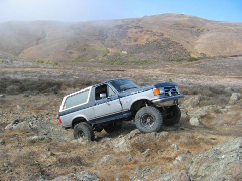 1989 Ford Bronco - A lifted Ford Bronco navigates a rocky trail with a hazy mountain in the background.