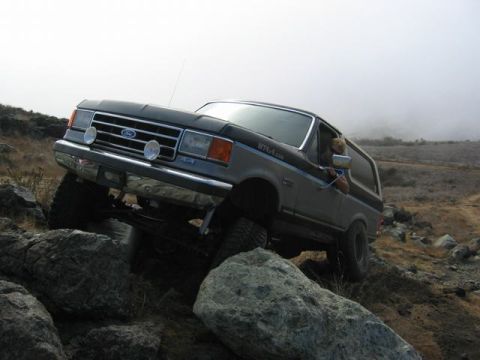 1989 Ford Bronco - A Ford Bronco navigates a rocky, off-road path with a foggy background.