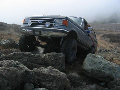 1989 Ford Bronco - A Ford Bronco navigates a rocky terrain with a foggy backdrop.