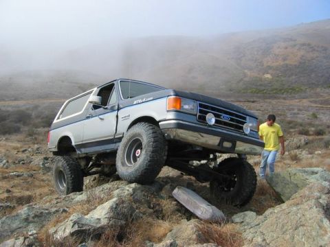 1989 Ford Bronco - This lifted 1989 Ford Bronco tackles a challenging rocky trail with a person walking nearby.
