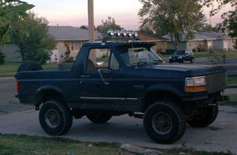 1995 Ford Bronco - Dark blue full-size Ford Bronco with the fiberglass rear top removed, parked at a suburban curb at dusk and shot from the passenger side. I…