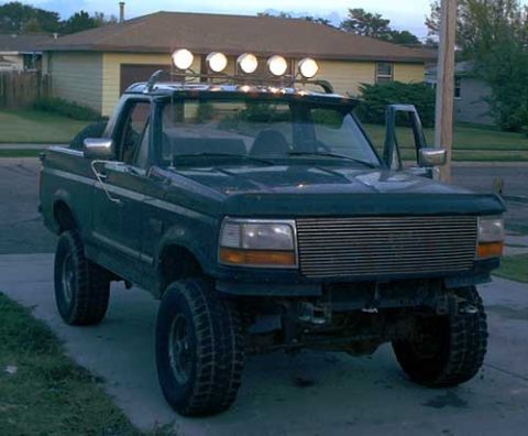1995 Ford Bronco - A dark green Ford Bronco with the top removed, parked on a driveway in a residential neighborhood at dusk. It has a lifted suspension with…