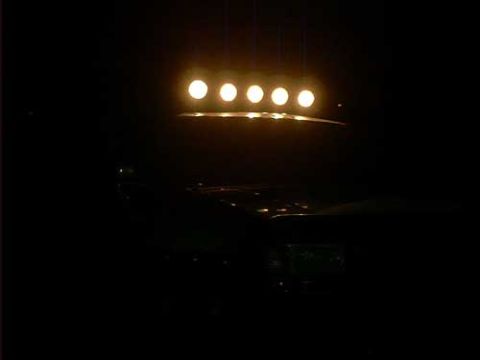1995 Ford Bronco - Night shot taken from inside a vehicle looking forward, showing five round amber-glowing lights on a roof-mounted light bar illuminated abo…