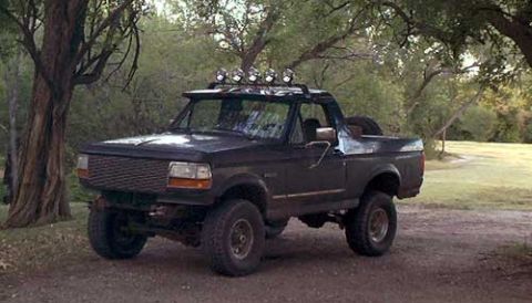 1995 Ford Bronco - Dark full-size Ford Bronco with the rear top removed, lifted on mud-terrain tires, wearing a windshield-header light bar with five round of…