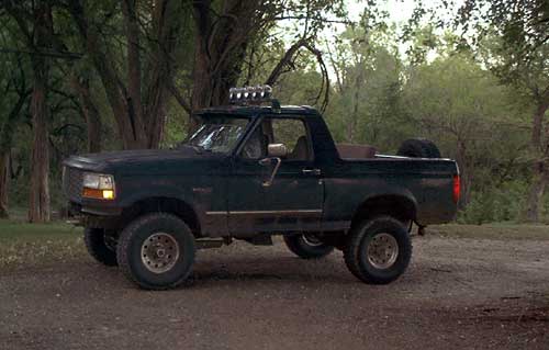 Dark green lifted Bronco, top off, roll bar light bar, parked on dirt