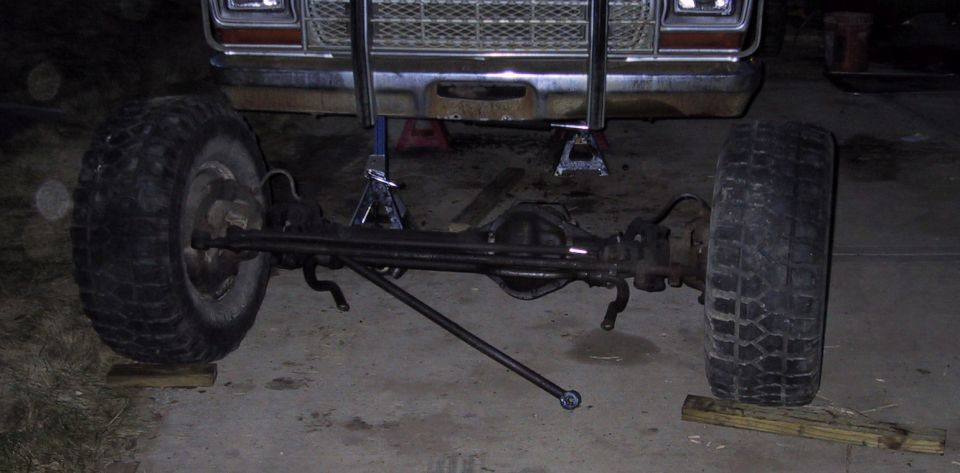 Solid front axle and steering on jack stands under a square-body truck in a garage