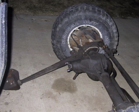 1983 Ford Bronco - A vehicle's front axle assembly and tire are shown resting on a concrete surface.