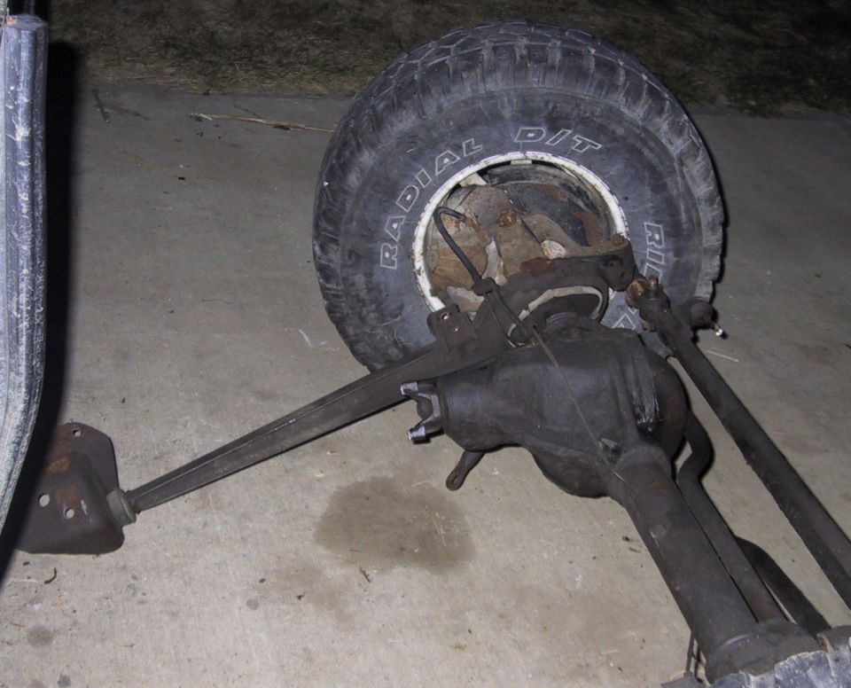 Removed solid front axle and differential lying on concrete near a spare tire