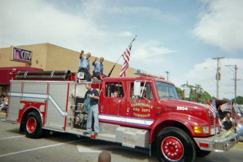 1998 Ford Crown Victoria - A fire truck with several people on board and standing on the side is participating in a parade.