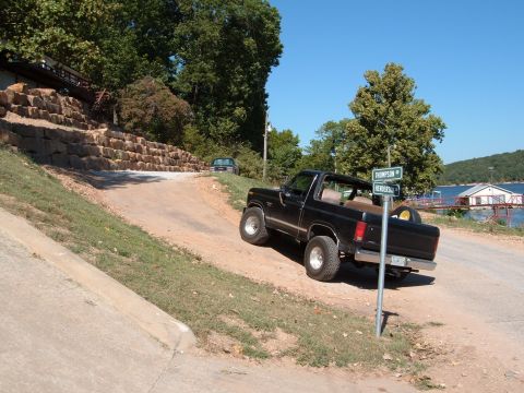 1986 Ford Bronco - A black Ford Bronco is parked on a dirt road near a lake, with a second vehicle in the distance.