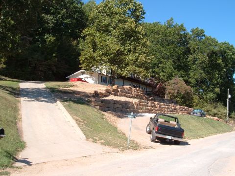 1986 Ford Bronco - A black 1986 Ford Bronco convertible is parked on a dirt driveway next to a house.