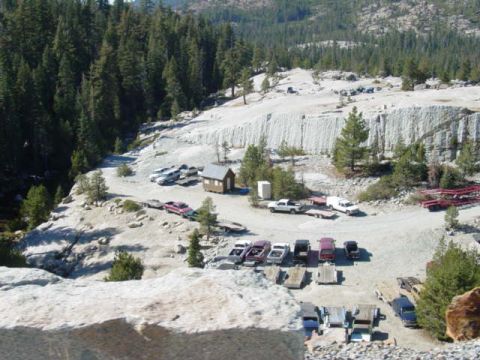 1986 Ford Bronco - A collection of vehicles are parked on a dusty road, surrounded by trees and a rocky quarry landscape.