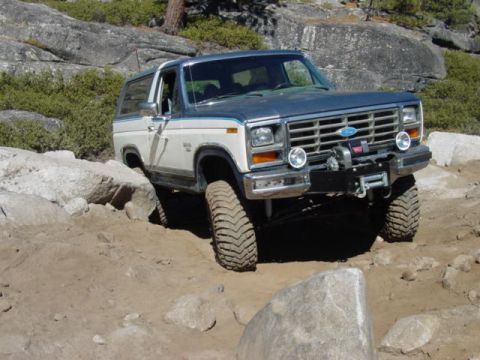 1986 Ford Bronco - A two-tone Ford Bronco navigates a rocky trail, demonstrating its off-road capability.