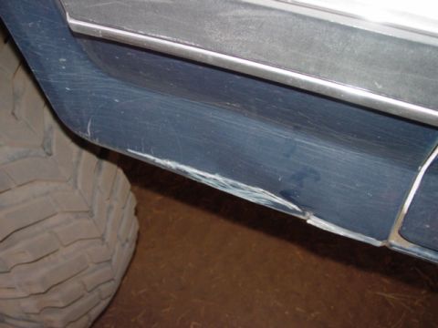 1986 Ford Bronco - The lower body panel of a vehicle shows extensive damage from off-roading, with a large tire visible.