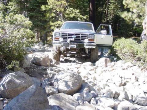 1986 Ford Bronco - 1986 Ford Bronco driving over large rocks on a wooded trail.
