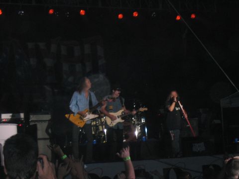 1988 Ford Bronco - A band plays a concert on a dimly lit stage, with red lights overhead and a crowd in the foreground.